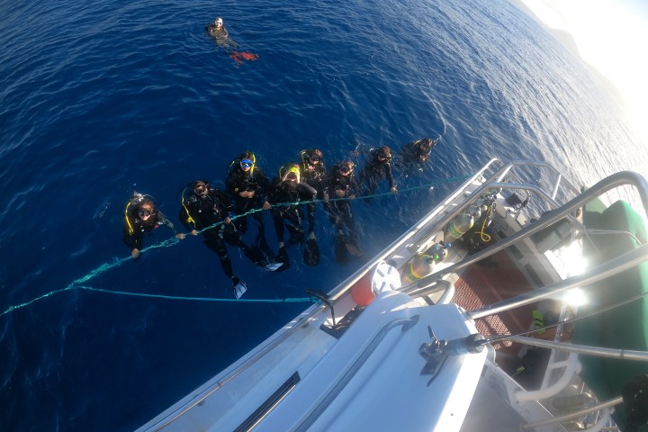 Divers in the ocean holding onto a rope near a boat.