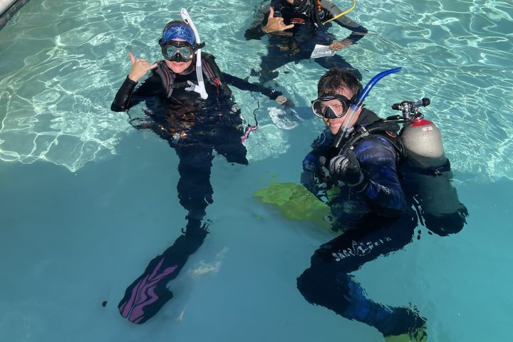 Three scuba divers in pool giving thumbs up signals.