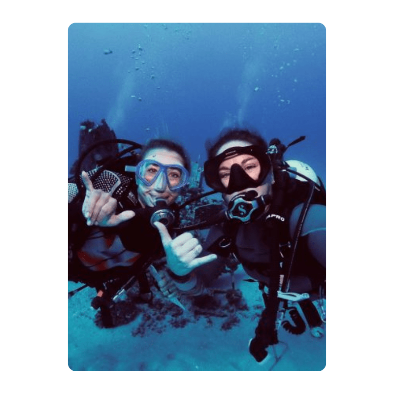 Two scuba divers underwater making hand gestures, wearing masks and gear.