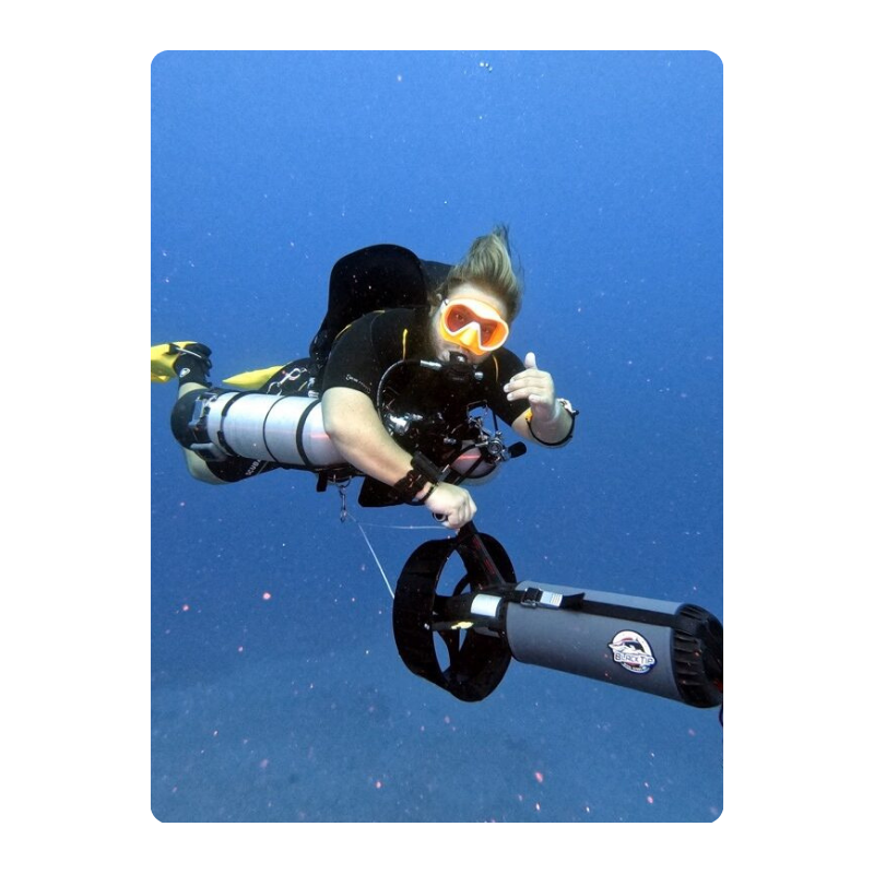 Diver underwater with gear and scooter, giving a thumbs up.