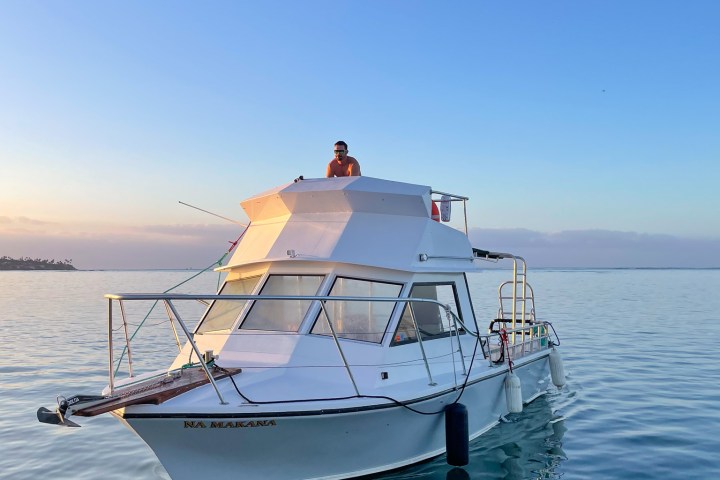 Person on a small white boat in calm water at sunset.