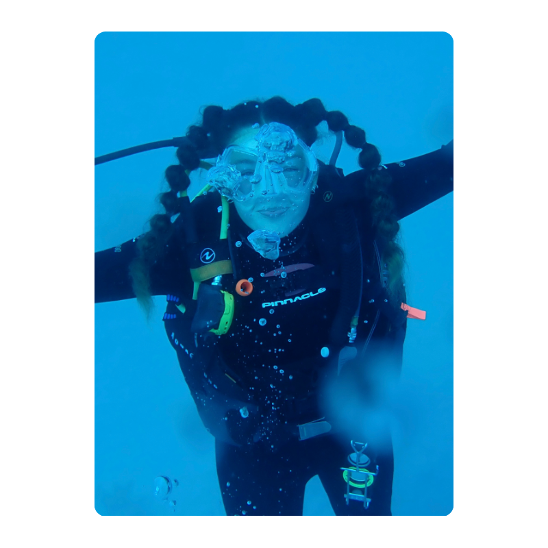 Scuba diver underwater, wearing gear and mask, with bubbles around.