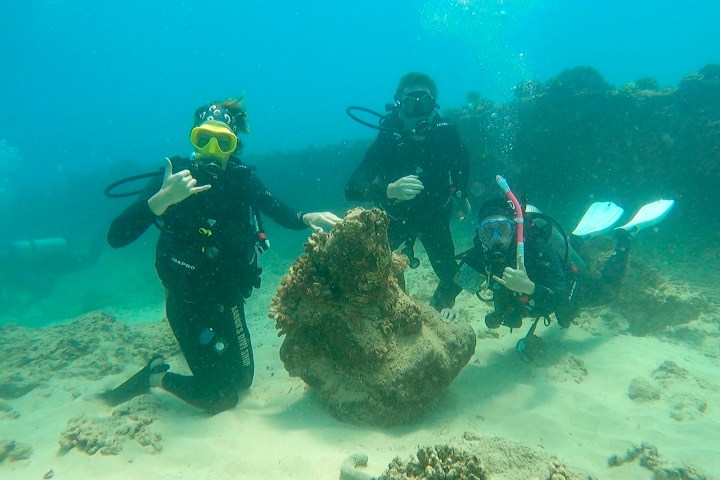 Three scuba divers pose underwater near a coral formation.