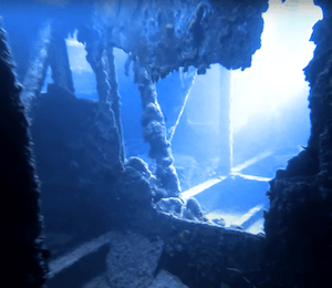 Interior of a sunken shipwreck illuminated by blue underwater light.