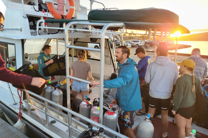 People on a boat preparing scuba gear at sunrise.