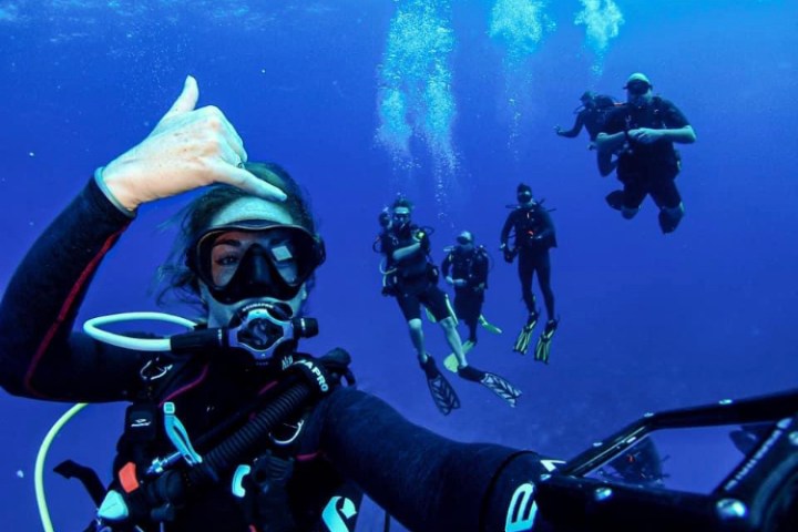 Scuba diver taking a selfie with a group of divers underwater.