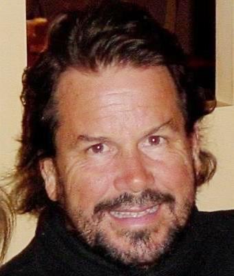 Middle-aged man with dark hair and a beard, smiling, wearing a black top.